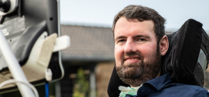 The picture shows Euan facing the camera and smiling with some houses in the background