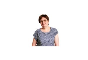 A white woman with dark hair and glasses wearing a patterned top in front of a white background.