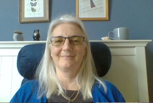 A middle aged white woman with white/blonde hair sitting against a head rest, smiling.