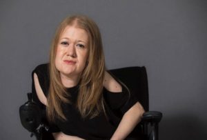 Young woman sat in a black wheelchair with a dark grey background