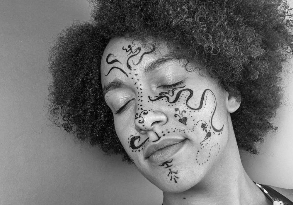 a black and white photograph of an afro-haired person with playful line drawings on their face