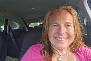 A white woman with strawberry blonde hair, wearing a bright pink top and smiling.