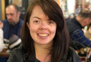 Head shot of Roseanne Scott who is sat at a table with her hands clasped together on the table. There is a cafÃ© ambience in the background. Roseanne is white with dark brown hair in a bob, she has a silver nose piecing ring and is wearing a leather jacket. â€¢ Image credit Roseanne Scott