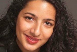 Headshoulder photo of Asian woman with long curly hair, in dark jacket and plain natural dark background.