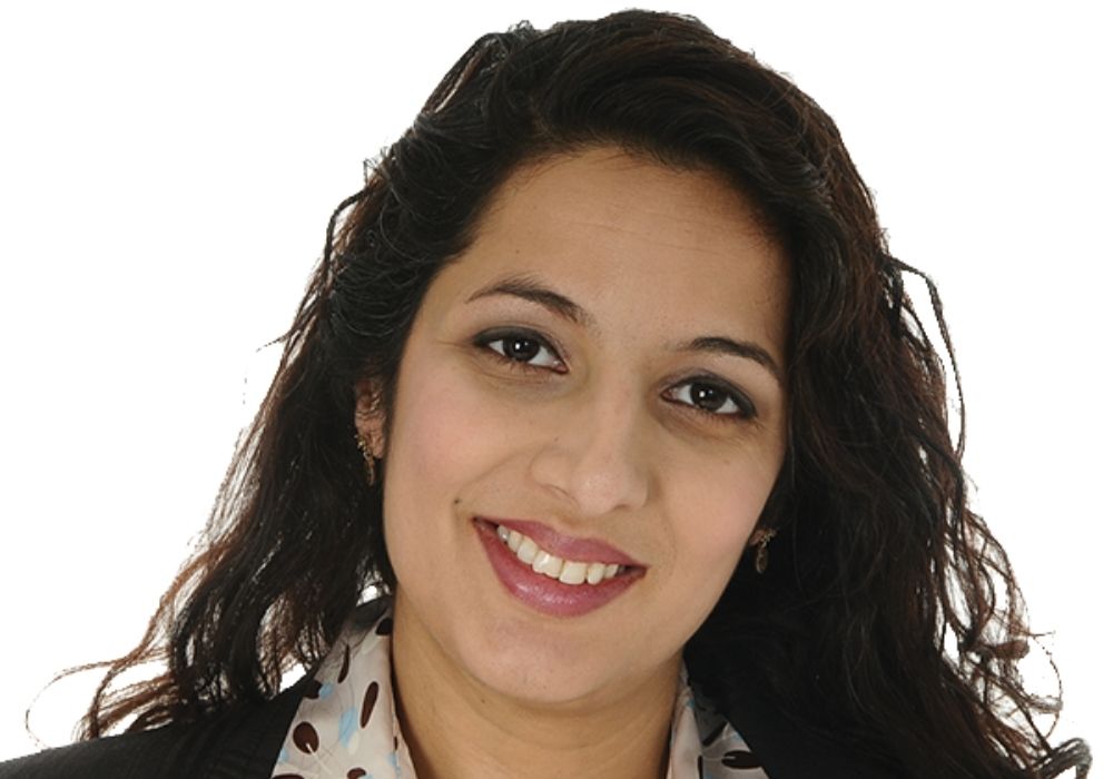 Headshoulder photo of Asian woman with long dark curly hair and white background.