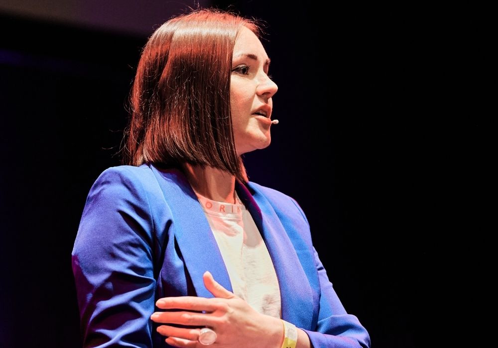 A white woman with brown bob cut hair is giving a talk.