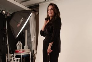 Christina is holding her white symbol cane, whilst being photographed against a white background.