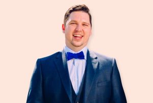 A dark haired man sat down wearing a blue three piece suit.