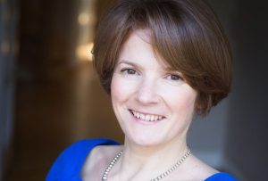 A smiling woman with short brown hair wearing a bright blue top