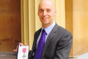 A wheelchair user in a suit showing his MBE medal