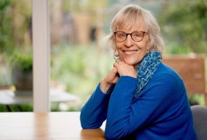 A light blond woman sitting in front of a window